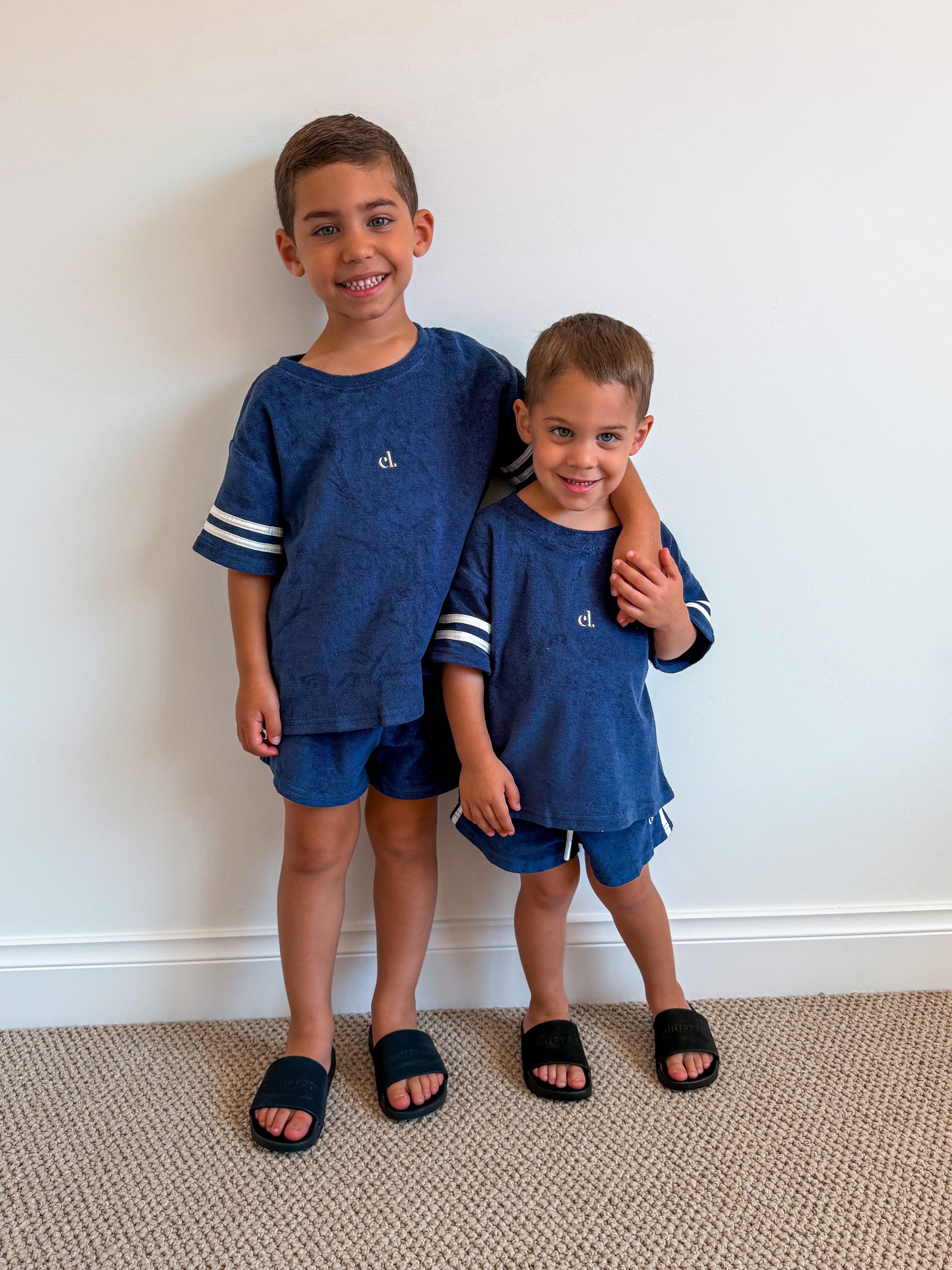Two young boys in matching navy Cami Lane Soft Terry Set outfits standing against a white wall.